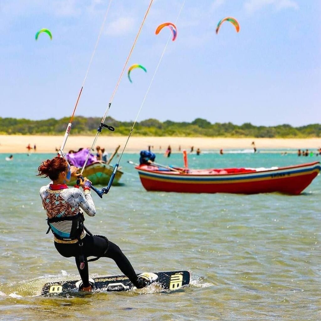 Uma pessoa praticando kitesurf, um esporte aquático radical que combina elementos de surfe, windsurf e wakeboard.