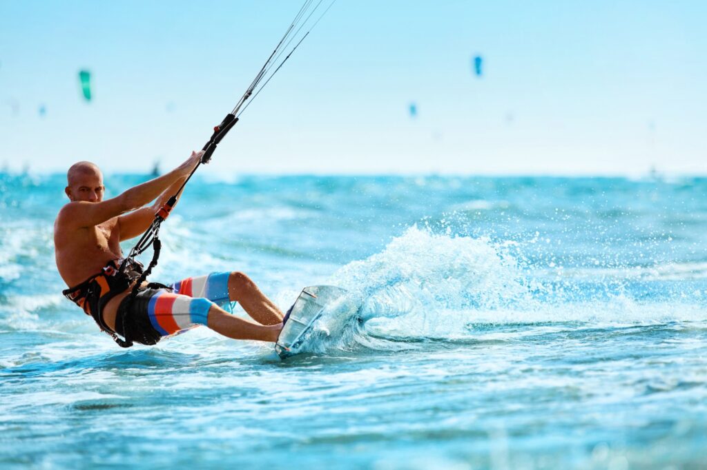 Uma pessoa praticando kitesurf, esporte aquático radical que utiliza a força do vento para impulsionar o praticante sobre a água. Uma pessoa praticando kitesurf, esporte aquático radical que utiliza a força do vento para impulsionar o praticante sobre a água.