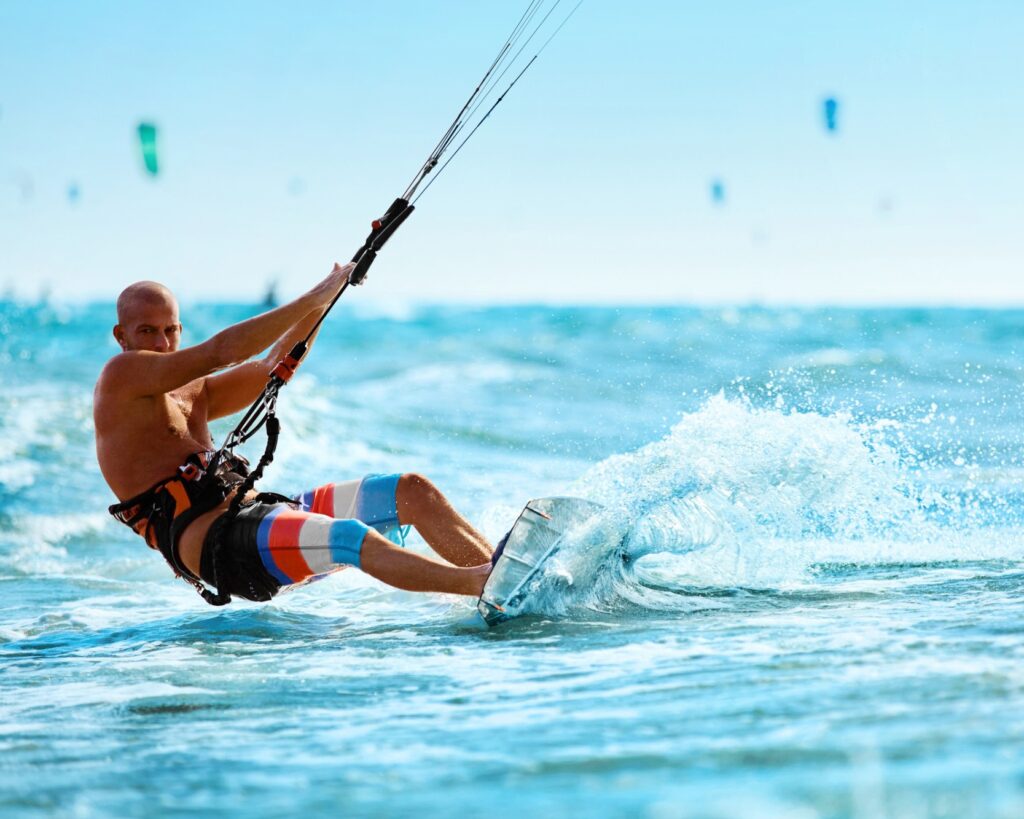 Uma pessoa praticando kitesurf, esporte aquático radical que utiliza a força do vento para impulsionar o praticante sobre a água.